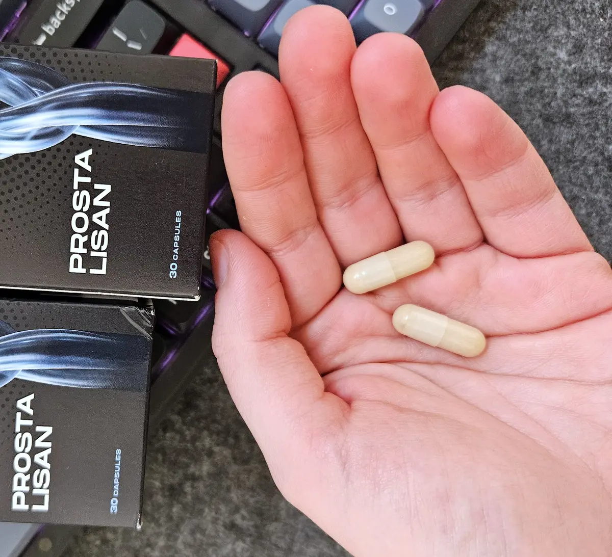 Capsule Prostalisan tari, bej deschis, în palmă, lângă cutiile originale